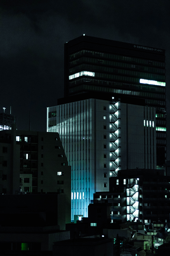 Distant cluster of buildings dimly lit by the street below and their outdoor staircases.